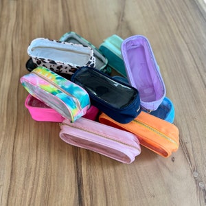 May include: A collection of clear zippered pouches in various colors and patterns, including tie-dye, leopard print, and solid colors. The pouches are made of a clear plastic material with a zipper closure.