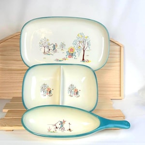 May include: A set of three off-white ceramic serving dishes with teal rims. The top rectangular platter, middle divided bowl, and bottom handled dish all feature a colorful illustration of a horse-drawn carriage and a park bench scene.