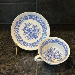 May include: A white teacup and saucer set with a blue floral design. The cup has a handle and the saucer has a scalloped edge. The floral pattern includes flowers and leaves.