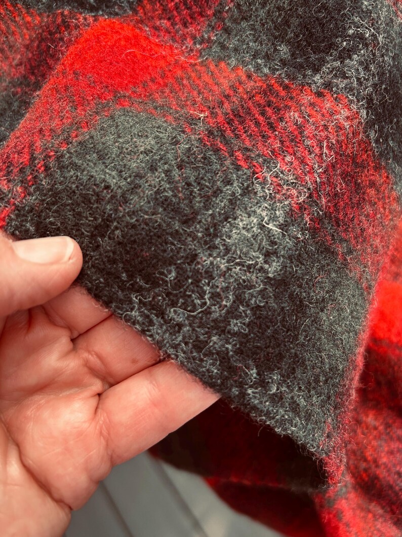 Pu&ograve; includere: Primo piano di un tessuto a quadri rosso e nero. Il tessuto ha un aspetto strutturato e sfocato. Il motivo &egrave; composto da audaci quadrati e linee rosse e nere. Il tessuto &egrave; probabilmente lana o un materiale simile.