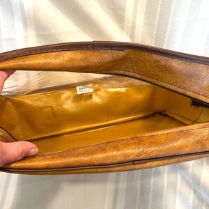 Pu&ograve; includere: Vista aperta di una valigia marrone vintage con interno dorato. La valigia ha un esterno strutturato con finiture marrone scuro e chiusura con cerniera. L'interno &egrave; di colore oro lucido. La valigia &egrave; aperta, rivelando l'interno.