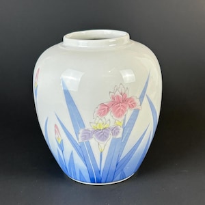 May include: White ceramic vase with a rounded shape, decorated with pink, purple, and yellow iris flowers and blue leaves. The vase has a glossy finish and a wide opening, perfect for displaying floral arrangements.