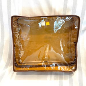Pu&ograve; includere: Una borsa portaoggetti rettangolare trasparente con finiture marroni simili alla pelle e interno giallo. La borsa &egrave; sigillata con una cerniera e sembra vuota. Ci sono due piccole etichette attaccate in alto.