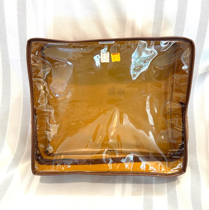 Pu&ograve; includere: Una borsa portaoggetti rettangolare trasparente con finiture marroni simili alla pelle e interno giallo. La borsa &egrave; sigillata con una cerniera e sembra vuota. Ci sono due piccole etichette attaccate in alto.