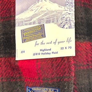 Pu&ograve; includere: Una coperta a quadri rossi e neri con un'etichetta che recita "Pendleton Woolen Mills". La coperta misura 132 x 178 cm e presenta il testo "Highland #810 Holiday Plaid". L'etichetta ha anche un'illustrazione di una montagna e alberi.