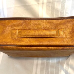 Pu&ograve; includere: Una borsa rettangolare marrone dorato con una superficie strutturata e un bordo marrone scuro. La borsa presenta una maniglia abbinata al centro ed &egrave; probabilmente realizzata in pelle o materiale simile alla pelle. La borsa &egrave; vuota.