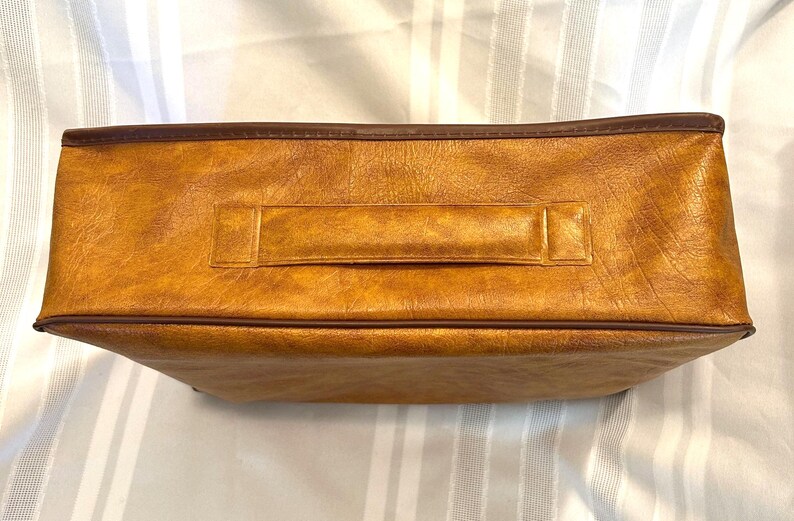 Pu&ograve; includere: Una borsa rettangolare marrone dorato con una superficie strutturata e un bordo marrone scuro. La borsa presenta una maniglia abbinata al centro ed &egrave; probabilmente realizzata in pelle o materiale simile alla pelle. La borsa &egrave; vuota.