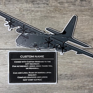 May include: A gray airplane sticker with a black and white border, and a black rectangle with white text that reads "CUSTOM NAME". The text below states the sticker can be customized with a message, logo, rank, or insignia.