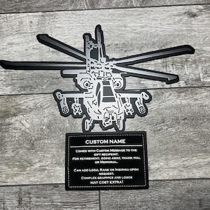 May include: A black metal silhouette of a helicopter with a silver finish. The helicopter is mounted on a black leather plaque with a white inscription that reads "CUSTOM NAME COMES WITH CUSTOM MESSAGE TO THE GIFT RECIPIENT. FOR RETIREMENT, GOING AWAY, THANK YOU, OR MEMORIAL CAN ADD LOGO, RANK OR INSIGNIA UPON REQUEST. COMPLEX GRAPHICS AND LOGOS MAY COST EXTRA!"