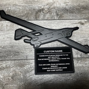 May include: Black metal silhouette of a plane with a white text box below. The text box says "CUSTOM NAME" and includes information about the product, such as the ability to add a custom message and logo.