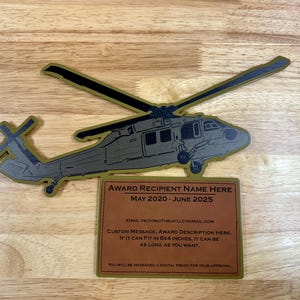 May include: A gold-colored wooden plaque with a black silhouette of a helicopter. The plaque has a brown leather-like insert with the text "AWARD RECIPIENT NAME HERE MAY 2020 - JUNE 2025" and an email address. The text "CUSTOM MESSAGE, AWARD DESCRIPTION HERE. IF IT CAN FIT IN 6X4 INCHES, IT CAN BE AS LONG AS YOU WANT." is also on the plaque.