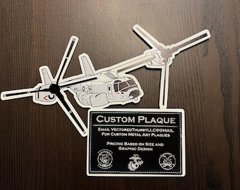 Könnte beinhalten: Ausgestanzte Aufkleber eines Militärhubschraubers und einer individuellen Plakette. Der Hubschrauber ist weiß und grau mit schwarzen Details. Die Plakette ist schwarz mit weißem Text "CUSTOM PLAQUE" und Kontaktinformationen.