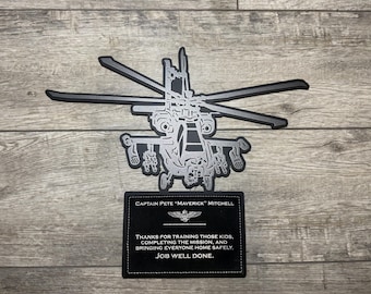 May include: A black and silver metal wall art piece featuring a detailed helicopter silhouette above a rectangular plaque. The plaque displays the text: Captain Pete "Maverick" Mitchell, an emblem, and the message: Thanks for training those kids, completing the mission, and bringing everyone home safely. Job well done.