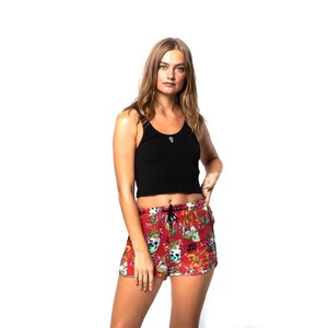 May include: A woman wearing a black tank top and red shorts with a floral and skull print.