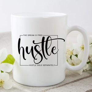 May include: White ceramic coffee mug with black text that reads "The dream is free - hustle - hustle sold separately".