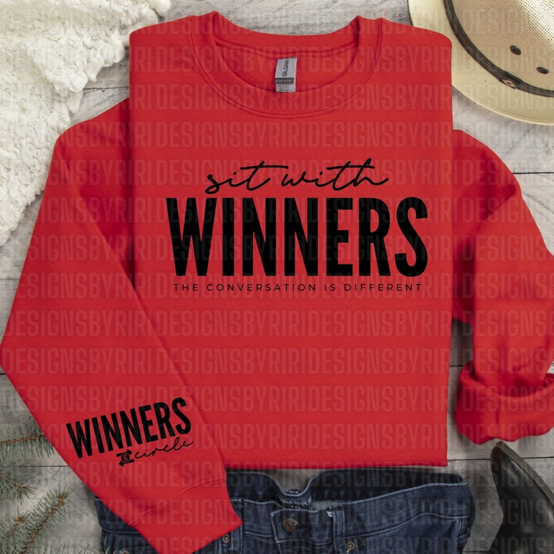 May include: Red sweatshirt with the text "Sit with Winners" and "The Conversation is Different" printed on the front. The left sleeve has the word "Winners" and the word "Circle" printed below it.