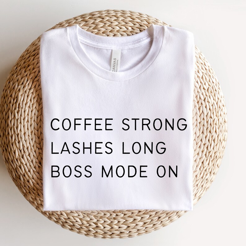 Op de afbeelding: Wit T-shirt met de tekst "COFFEE STRONG LASHES LONG BOSS MODE ON" erop gedrukt.