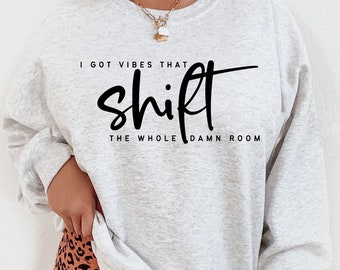 May include: A gray sweatshirt with the text "I got vibes that shift the whole damn room" printed in black.