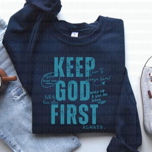 May include: A navy blue sweatshirt with the text "Keep God First Always" in teal blue lettering. The text is styled with a distressed look. There are additional phrases in smaller teal blue lettering around the main text, including "Spirit lead me", "Live to please him!" and "Talk to him often".