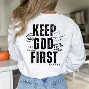 May include: White long-sleeved sweatshirt with black text that reads "KEEP GOD FIRST ALWAYS". The text is surrounded by smaller text that reads "spirit lead me", "talk to him often", "live to please him!" and "wake up & give me Jesus".