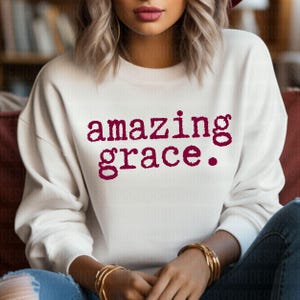 May include: White sweatshirt with the words "amazing grace" printed in maroon.