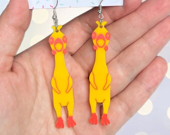 May include: A pair of yellow rubber chicken earrings with red feet and eyes. The earrings are hanging from silver hooks and are on a white card with the text "folksy love" in pink letters.