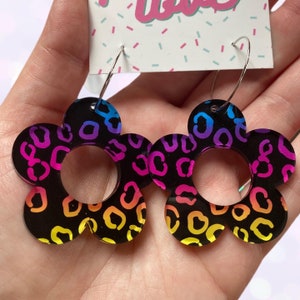 May include: A pair of rainbow gradient flower-shaped hoop earrings with a black leopard print pattern.