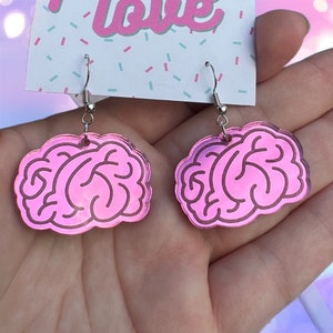 May include: A pair of pink iridescent earrings shaped like a human brain. The earrings are on a silver hook.