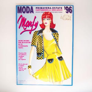 Op de afbeelding: Een vintage modetijdschriftcover met een vrouw die een gele jurk draagt met een zwart-wit geblokt jasje. Het tijdschrift heet "Moda Marly" en de tekst "Primavera-Estate '96 Cartamodelli Esclusivi" is zichtbaar op de cover.