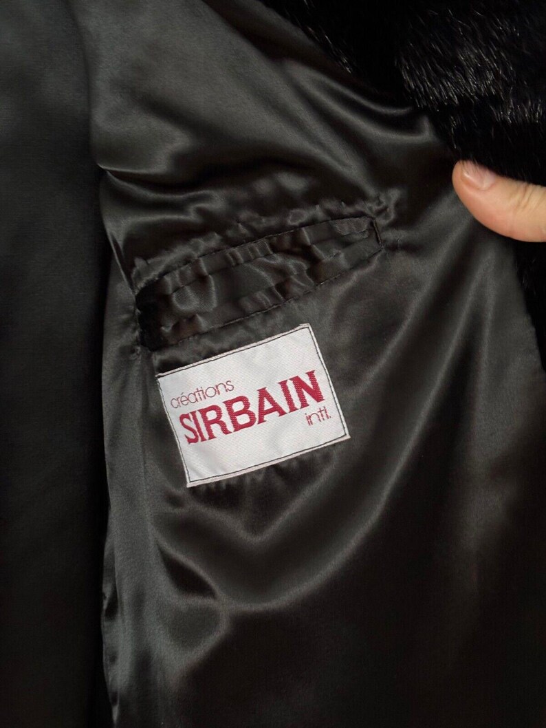 Puede incluir: Un abrigo de piel negro con forro de sat&eacute;n negro. El forro tiene un bolsillo con una etiqueta blanca que dice "cr&eacute;ations SIRBAIN int'l".