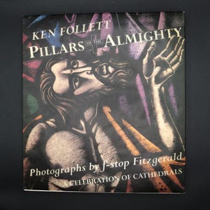 Könnte beinhalten: Buchcover für "Pillars of the Almighty" von Ken Follett. Das Cover zeigt ein Buntglasfensterbild einer Person mit erhobenen Armen. Der Text "Photographs by f-stop Fitzgerald" und "A Celebration of Cathedrals" ist ebenfalls auf dem Cover.