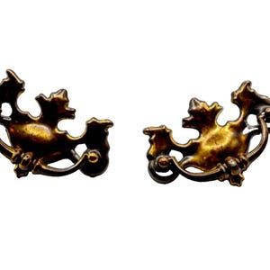 以下が含まれることがあります： 装飾的な葉のデザインが施されたアンティークブラスのキャビネットプル2個。プルは、湾曲したハンドルが付いたスタイリッシュな葉の形をしています。