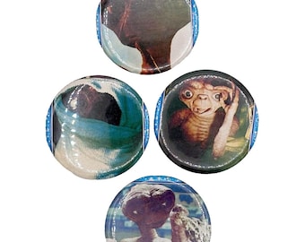 Peut inclure: Ensemble de quatre badges ronds en forme de bouton représentant des images du personnage extraterrestre E.T. du film E.T. l'extraterrestre. Les badges sont bleus et blancs avec une finition brillante.