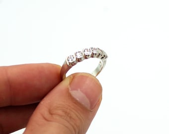 Könnte beinhalten: Ein silberner Ring mit einer Reihe von klaren Zirkonia-Steinen, die in einem wellenförmigen Band gefasst sind.
