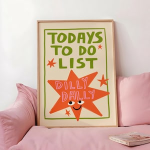May include: A rectangular framed wall art print featuring the green text TODAYS TO DO LIST and a large orange star with a smiling face and the pink text DILLY DALLY inside. The design includes small red stars and a green border on a cream background.