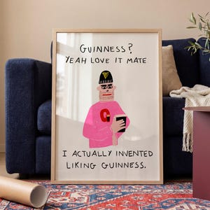 Könnte beinhalten: Ein gerahmter rechteckiger Druck mit einer Cartoon-Illustration einer Person, die eine schwarze Mütze und einen rosa Pullover mit einem roten Buchstaben G trägt. Der Text lautet: GUINNESS? YEAH LOVE IT MATE. I ACTUALLY INVENTED LIKING GUINNESS. Heller Holzrahmen.