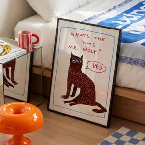 May include: A framed wall art print featuring a dark brown wolf illustration with blue glasses. The text reads, "WHATS THE TIME MR. WOLF?" and a speech bubble says "BED". The artwork is outlined in a light blue border on a white background.