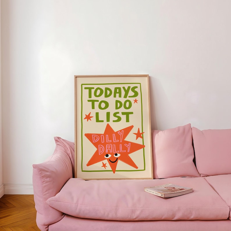 May include: A rectangular framed wall art print featuring the green text TODAYS TO DO LIST and a large orange star with a smiling face and the pink text DILLY DALLY inside. The design includes small red stars and a green border on a cream background.