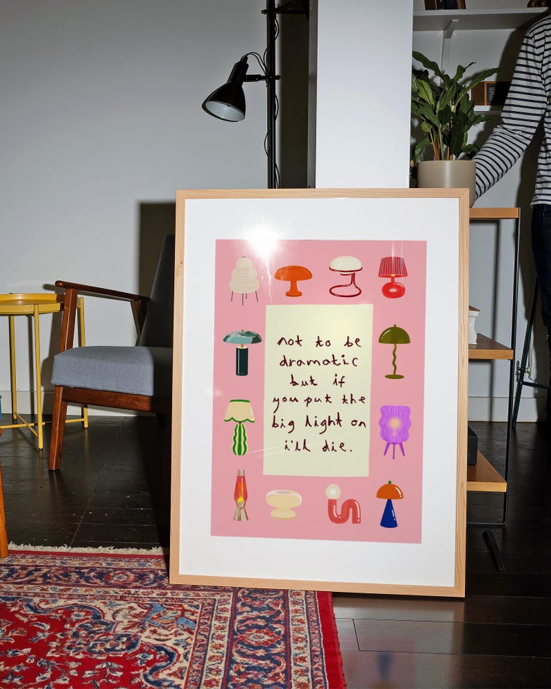 May include: A framed rectangular print with a pink background featuring various colorful lamp illustrations surrounding a central pale yellow rectangle containing the black handwritten text: not to be dramatic but if you put the big light on i'll die.