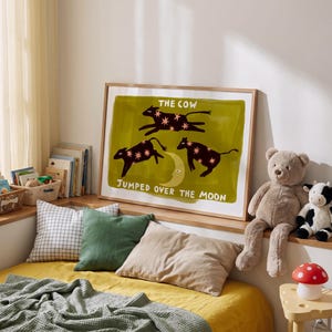 May include: A framed rectangular wall art print featuring a dark olive green background with three black cow silhouettes decorated with pink stars, a yellow crescent moon, and the white text THE COW JUMPED OVER THE MOON.