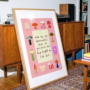 May include: A framed rectangular art print with a pink background featuring various colorful lamp illustrations surrounding a central cream-colored rectangle with the handwritten text: not to be dramatic but if you put the big light on i'll die.