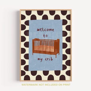 May include: A framed art print with a brown crib illustration on a light blue background, with the words "welcome to my crib." The print has a brown and cream polka dot border.