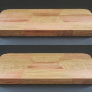 Peut inclure: Deux planches à découper rectangulaires en bois. Les planches sont faites de bois clair et foncé, avec des coins arrondis. Le grain du bois est visible, et elles sont présentées sur un fond gris.