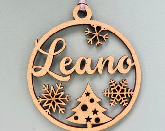 May include: A wooden Christmas bauble with the name "Leano" cut out in the centre. The bauble is decorated with a Christmas tree and snowflakes.