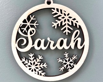 May include: A round wooden bauble with a snowflake design and the name "Sarah" cut out in the centre.