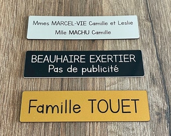 May include: Three rectangular nameplates with black text on a white, black, and gold background. The top nameplate reads "Mmes MARCEL-VIE Camille et Leslie Mlle MACHU Camille". The middle nameplate reads "BEAUHAIRE EXERTIER Pas de publicité". The bottom nameplate reads "Famille TOUET".