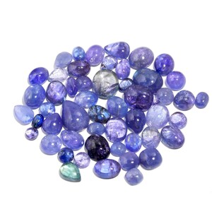May include: A collection of blue and purple gemstones, likely Tanzanite, in various shapes and sizes. The gemstones are arranged in a loose pile on a white background.