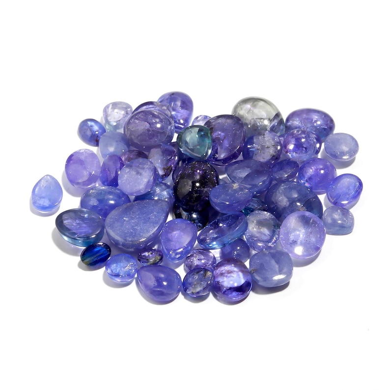 May include: A collection of various sized and shaped blue gemstones, including oval, round, and teardrop shapes. The gemstones are arranged in a pile on a white background.