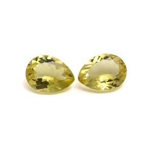 Może przedstawiać: Dwa żółte kamienie szlachetne w kształcie gruszki z fasetkami. Kamienie szlachetne znajdują się na białym tle.