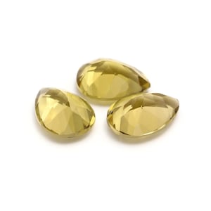 Może przedstawiać: Trzy fasetowane, żółte kamienie szlachetne w kształcie gruszki. Kamienie szlachetne są półprzezroczyste i mają jasnożółty kolor.